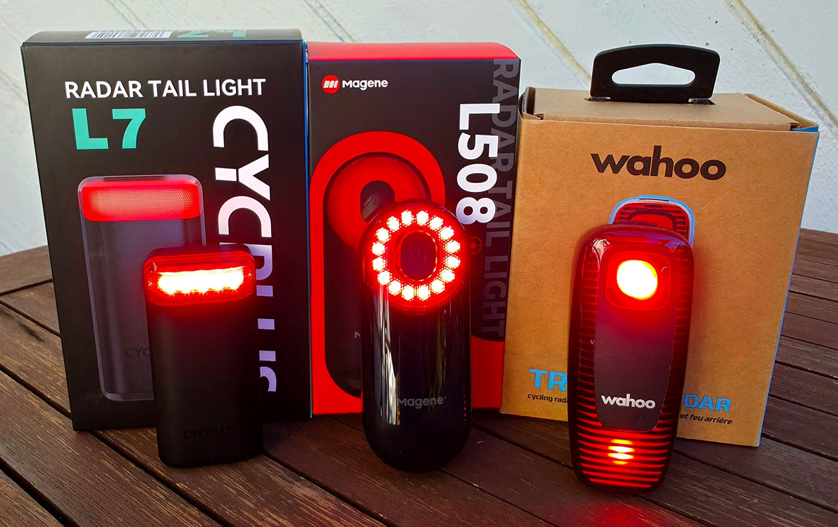 CYCPLUS L7-, Magene L508- ja Wahoo TRACKR RADAR -takatutkat valot päällä pakkauksiensa edessä puisella pöydällä.