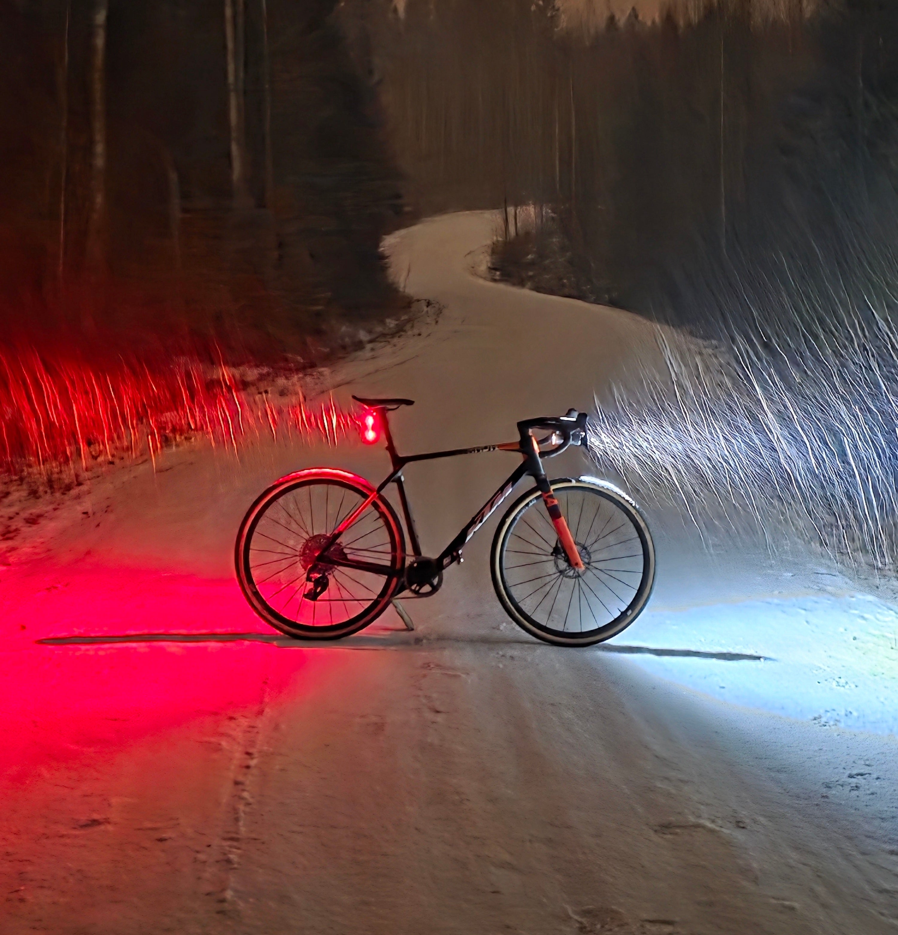 Pimeässä pyöräily. Pyörä pimeässä talvella lumisessa maastossa jossa lunta sataa. Edessä Exposure Toro 16 valaisin ja takana Wahoo Trackr Radar takavalo ja tutka
